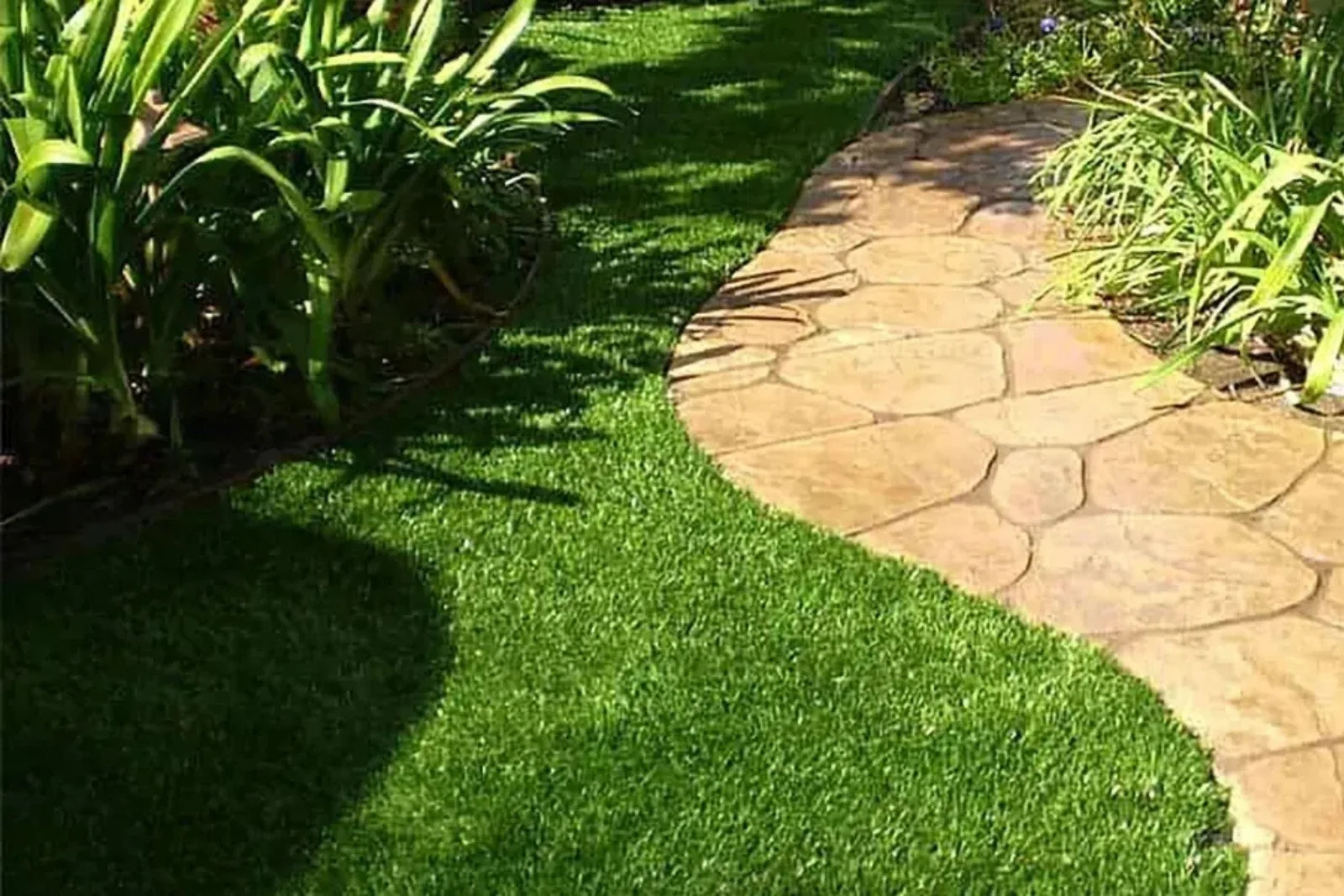 Artificial lawn turf in a lush green color creates a low-maintenance and durable landscaping solution, with a curving stone pathway and natural greenery