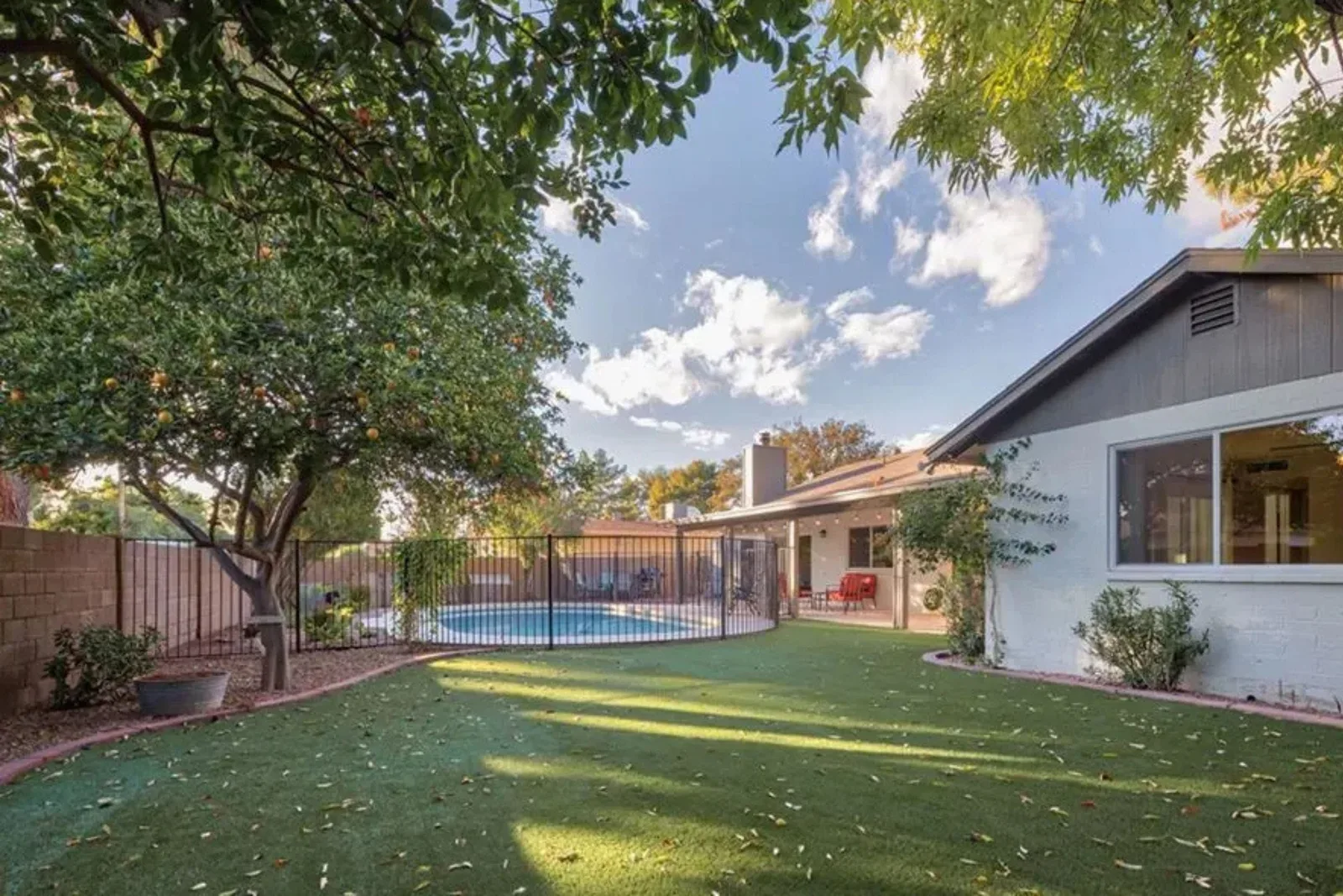 Artificial grass lawn creates a lush, vibrant green, and low-maintenance backyard, offering a drought-friendly landscaping solution with a swimming pool and patio.